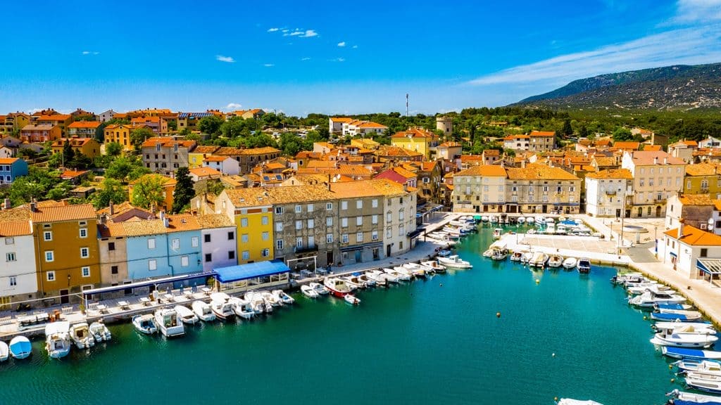 Colorful boats and pastel Venetian architecture in the harbor of Cres Town, Croatia.