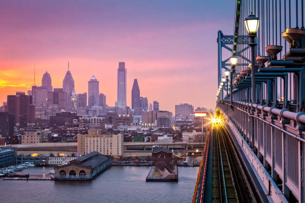 philadelphia skyline at dusk with ben franklin bridge and train coming under purple hazy sky