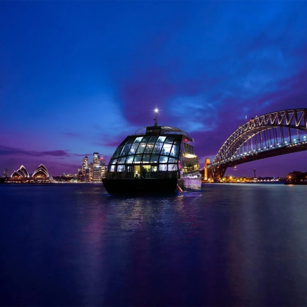 Night-time Sydney Harbour dinner cruise with the Opera House and Harbour Bridge lit up in the background.
