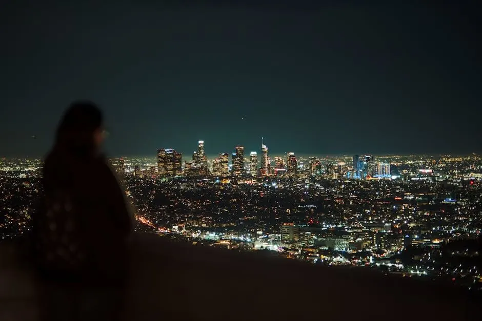 A breathtaking view of the illuminated Los Angeles skyline at night with a blurred person in the foreground.